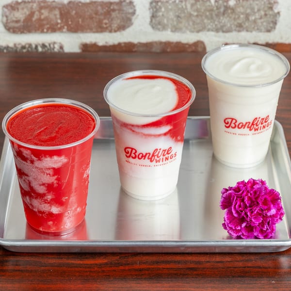 Three Bonfire Wings frozen drinks, two red and white, one white, on a metal tray with a pink flower.