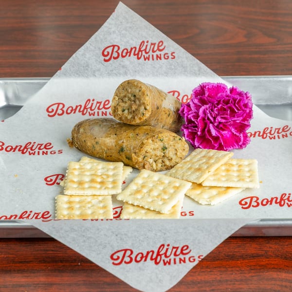 Two Bonfire Wings boudin sausages with crackers and a pink flower on branded paper.