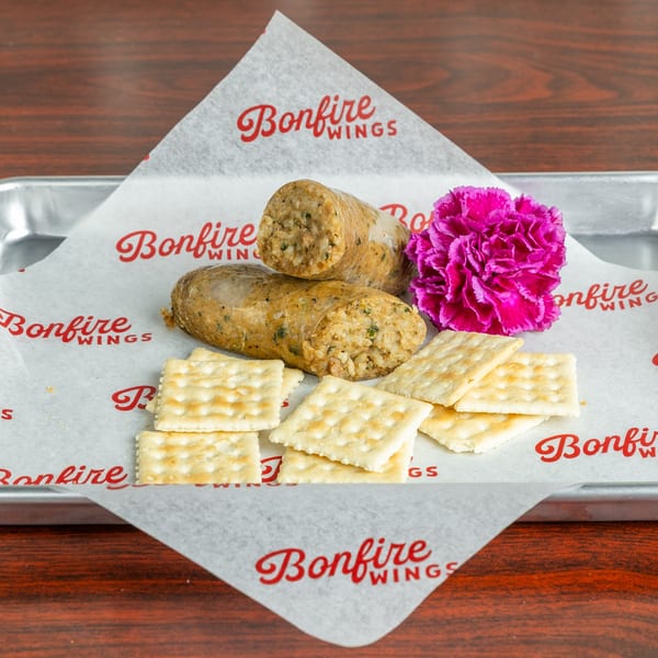 Two Bonfire Wings boudin links, crackers, and a pink flower on branded wax paper.