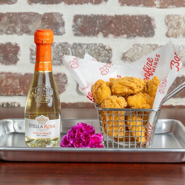 Bonfire Wings' fried chicken bites in a metal basket with a bottle of Stella Rosa Peach wine.