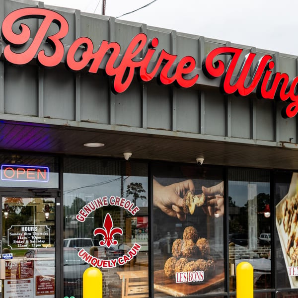 Exterior of Bonfire Wings restaurant with a red neon sign and window decals advertising Creole Cajun food.