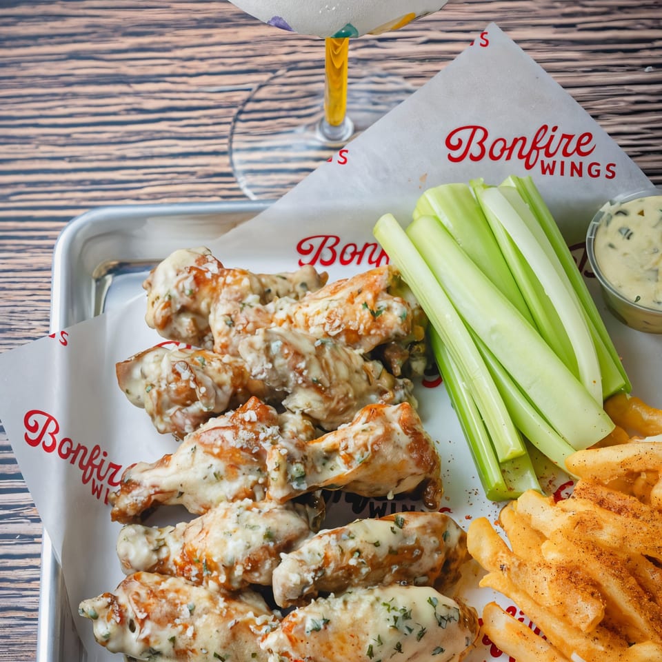Bonfire Wings' garlic parmesan wings, fries, celery sticks, and dipping sauce on a metal tray.