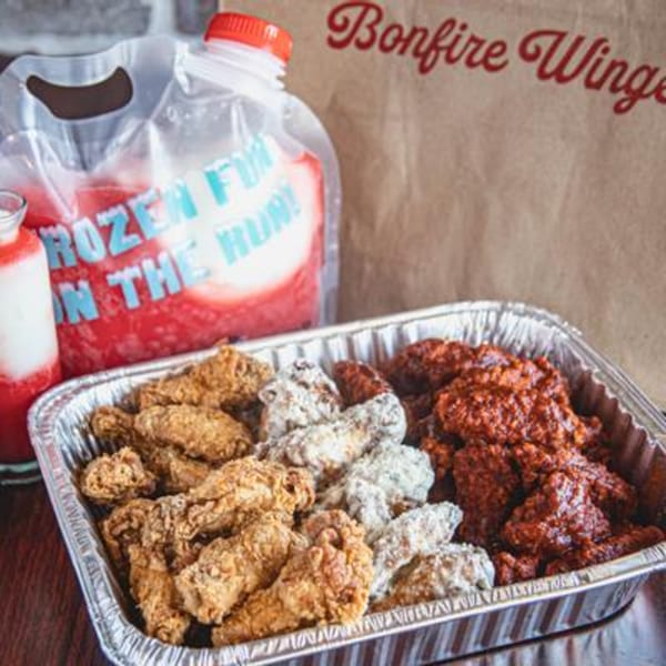 Bonfire Wings take-out with three flavors of wings in a foil pan and a frozen drink pouch.