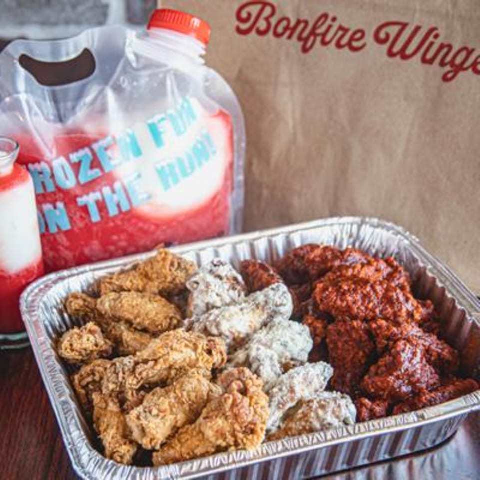 Bonfire Wings take-out with three flavors of wings in a foil pan and a frozen drink pouch.