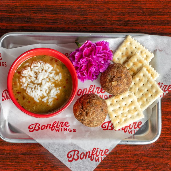 Bonfire Wings' gumbo with rice, two boudin balls, and crackers on a metal tray.