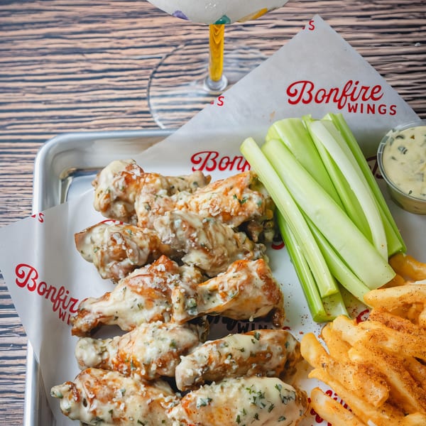 Bonfire Wings' garlic parmesan wings, fries, celery sticks, and dipping sauce on a metal tray.