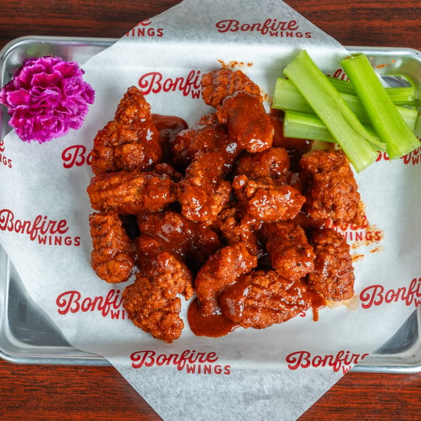 Bonfire Wings' saucy boneless wings with celery sticks and a purple flower on a metal tray.