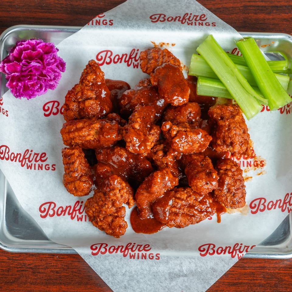 Bonfire Wings' saucy boneless wings with celery sticks and a purple flower on a metal tray.