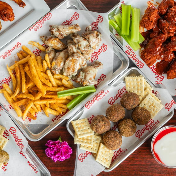 Multiple trays of Bonfire Wings, including garlic parmesan wings, buffalo wings, fries, and hush puppies.