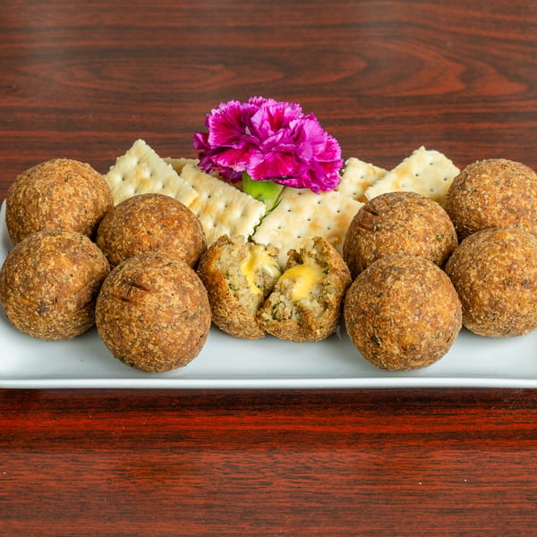 A platter of Bonfire Wings' fried boudin balls with crackers and a purple flower garnish.
