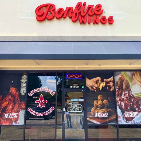 Bonfire Wings restaurant storefront with red signage, an 'OPEN' neon sign, and window decals of wings.
