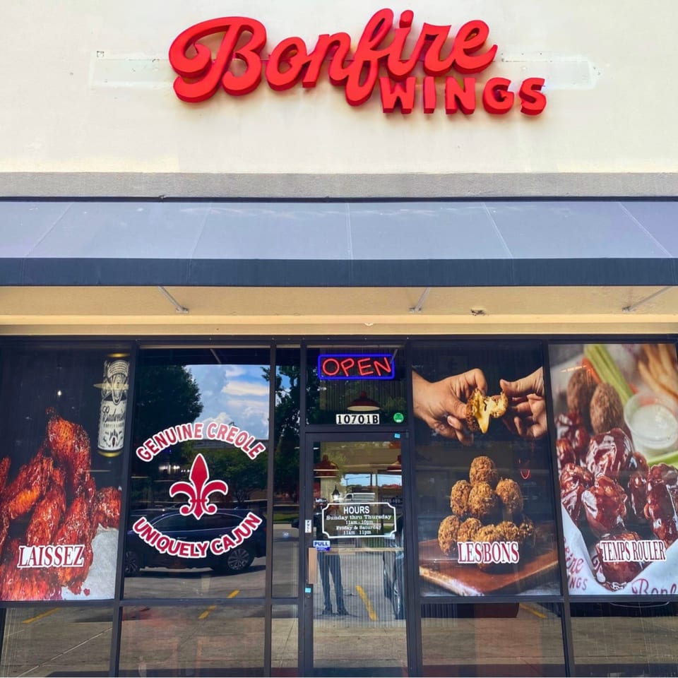 Bonfire Wings restaurant storefront with red signage, an 'OPEN' neon sign, and window decals of wings.